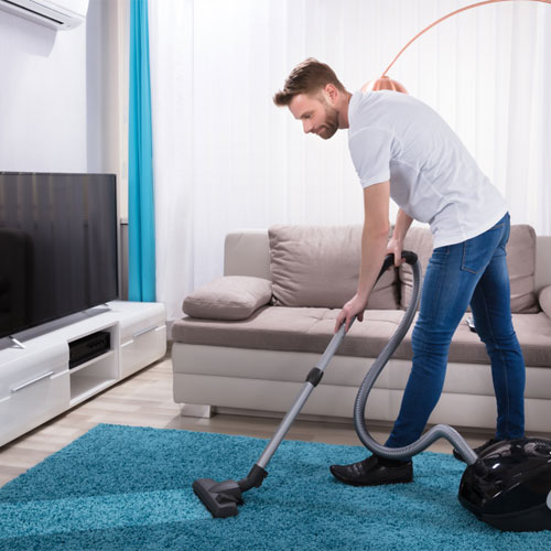 deep-cleaning-carpet-vacuum-twice-both-ways-columbia-sc Man vacuuming his living room with bright blue carpet.